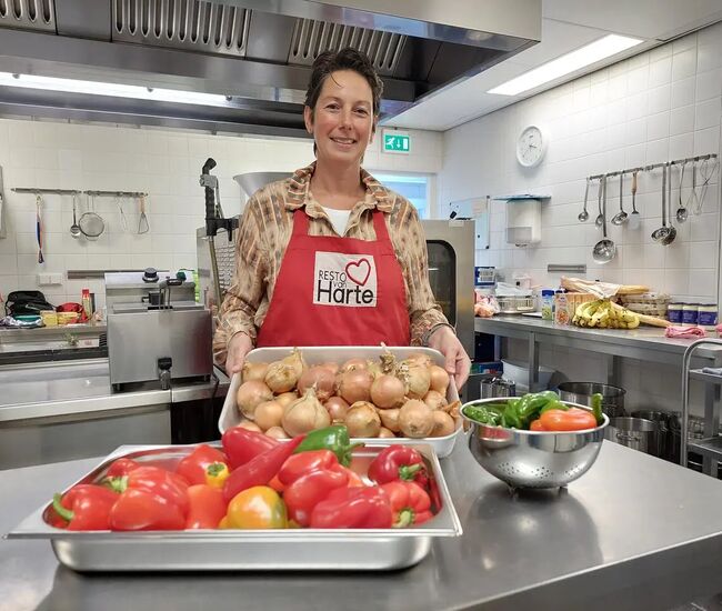 Vrouw in een keuken met groenten en een schort, glimlachend.