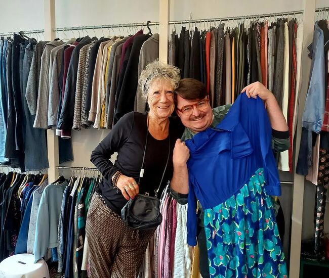 Twee blije mensen poseren met een kleurrijke jurk in een kledingwinkel.