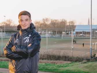 Jonge man in sportjack met voetbalveld op de achtergrond.