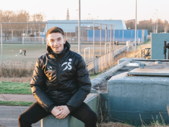 Jongeman in sportjack met een voetbalveld op de achtergrond.