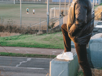 Jongeman in sportoutfit kijkt naar een voetbalveld bij zonsondergang.