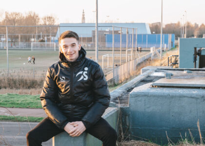 Jongeman in sportjack met een voetbalveld op de achtergrond.