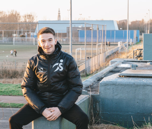 Jongeman in sportjack met een voetbalveld op de achtergrond.