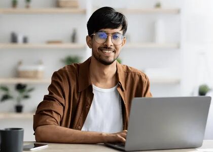 Jonge man met een laptop, glimlachend in een moderne werkomgeving.