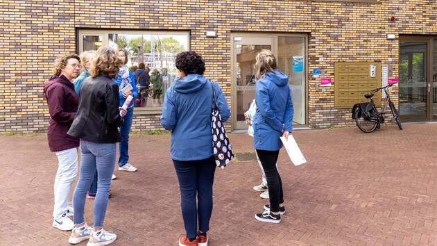 Groep mensen staat buiten een gebouw en praat met elkaar.