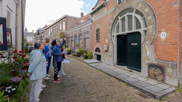 Groep mensen kijkt naar een versierde gevel in een straat.