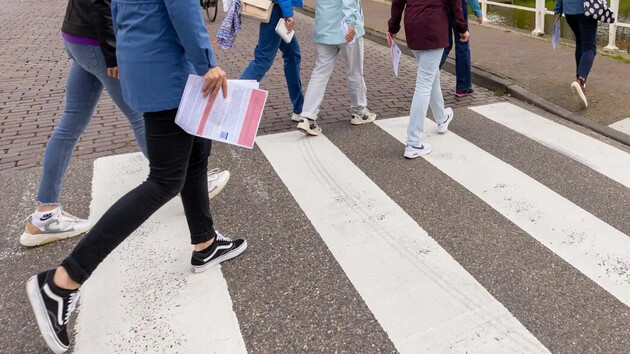 Groep mensen steekt een zebrapad over met papieren in de hand.