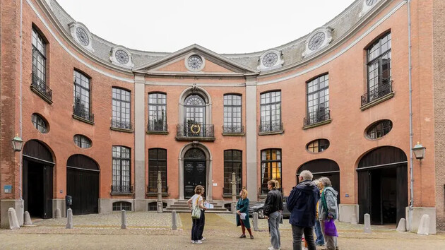 Groep mensen voor een historische, ronde gevel met grote ramen.