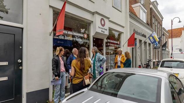 Groep mensen voor een tweedehands winkel met rode vlaggen.