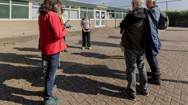 Groep mensen staat buiten bij een sportcomplex, in gesprek.